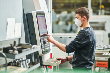 Industrial worker operating cnc machine in protective mask at metal machining industry