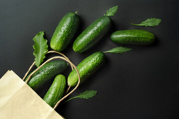 Cucumbers and herbs fell out of a paper bag on a black background. GMO free. Vegetarian meal from the market. Top view on dark concrete table background. copy space. Bag with fresh cucumbers