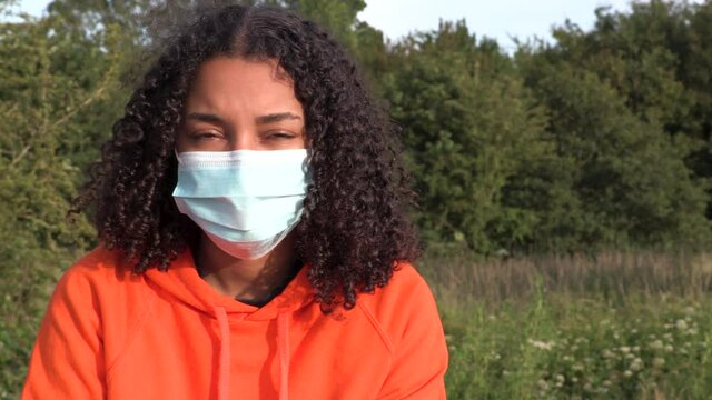 Beautiful mixed race African American girl biracial teenager young woman outside wearing a face mask during COVID-19 Coronavirus pandemic