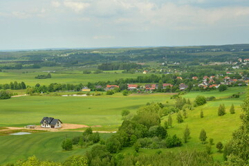 View of a hilly area full or meadows, forests, and small villages seen from the top of a tall hill on a cloudy yet warm summer day on a Polish countryside