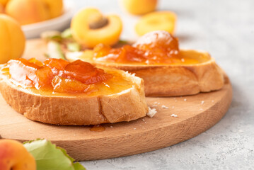 Toast of bread and apricot jam with slices of fruit and fresh apricots on the table. Toasts with jam close-up. Tasty sweet breakfast.