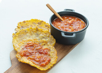 Pot with fried tomato accompanied by fried banana on a white background. Typical dish of Colombian cuisine. Copy space. Patacón con hogao.