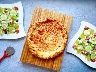 Top down view of freshly baked deep pan cheese and tomato pizza with a side dish of fresh feta...