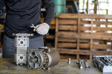 Professional mechanic man inspection hydraulic gear pump of wheel loader in workshop, repair maintenance heavy machinery