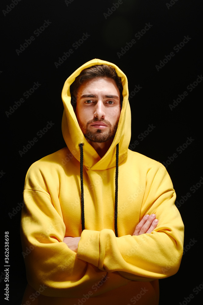 Wall mural A young man of 25-30 years old in a yellow sweatshirt stands against a black wall. 