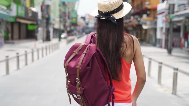 Carefree young brunette woman smiling and walking down street on vacation with backpack