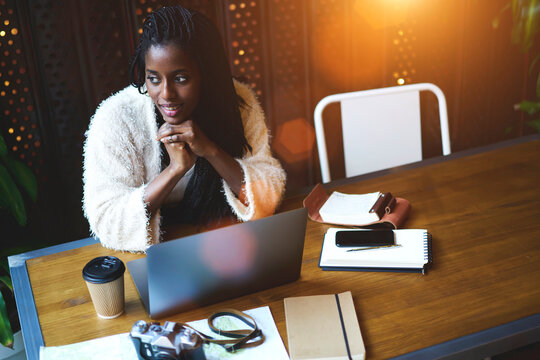 Beautiful afro american female in casual clothes enjoying free time sitting at table in cafe indoors with digital devices,charming trendy hipster girl thinking about working plan for startup project