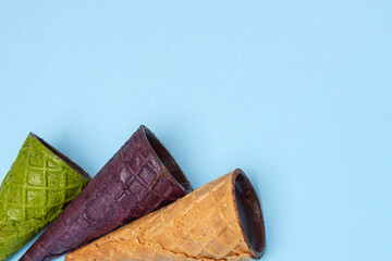 Top view of waffle horns in chocolate glaze placed next to each other from the left corner  on pale blue background, flat lay. Green, purple, brown. Waffle dessert, close up, copy space