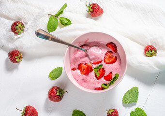 Strawberry ice cream in a white bowl with strawberries on a white wooden background