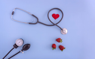 doctor's stethoscope, blood pressure monitor, strawberry on a blue background. the concept of medicine and healthy food