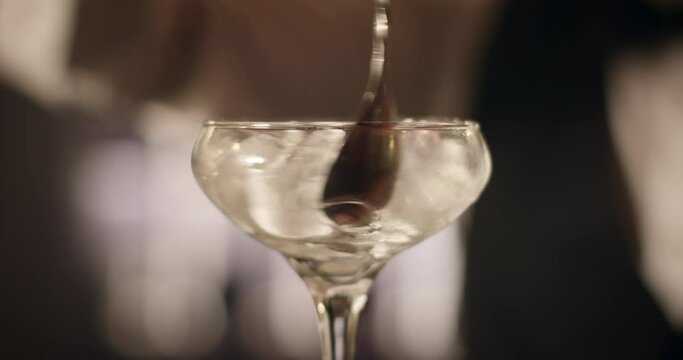 Close-up shooting. Bartender is turning the ice in glass using the bar spoon. 4k