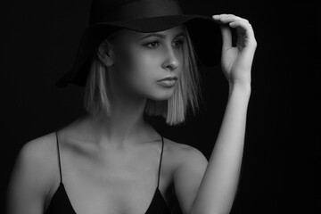 Black and white portrait blondes on a black background in a hat and Tank Top With Thin Straps. holding the brim of his hat with his hands