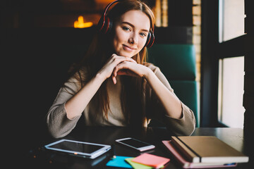 Portrait of charming student with modern headphone on head looking at camera and smiling. teenager listening music via earphones and enjoying  time sitting in coffee shop