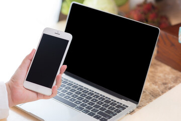 Hand using blank screen mobile smart phone,  working on laptop computer over shoulder view