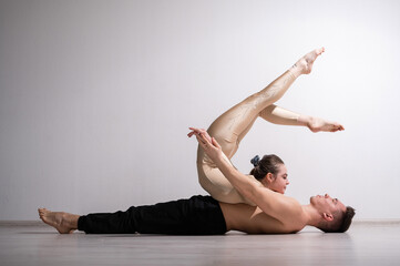Obraz premium Acrobatic couple perform number on a white background. A duet of gymnasts rehearsing a performance with support. A man and a very flexible woman are dancing.