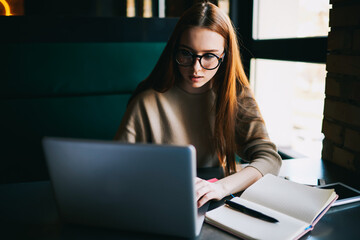 Concentrated female copywriter in eyeglasses installing software on digital computer with free 4G...