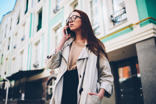 Attractive confident female dressed in casual outfit having mobile conversation using application on telephone.Pretty hipster girl communicating with friends via modern gadget while strolling