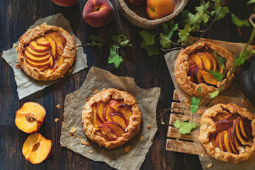 Homemade tart peach Galette (French name) - a few open pies with fresh organic fruits, rustic kitchen, dark wooden table. Low key shot. Natural light, copy space, selective focus.