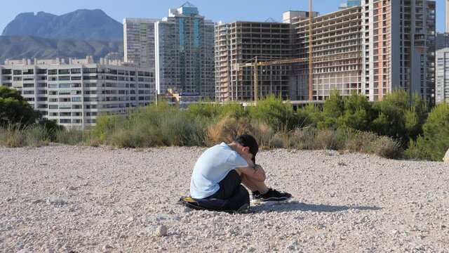 Sad unhappy boy sitting alone hugging his knees outdoors. Child depression, abuse, children problems concept