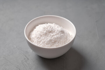 Coconut shavings in a white bowl on a concrete table
