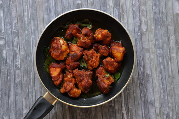 Chicken fry or Fried chicken kabab which is well garnished with curry leaves in a black frying pan with grey background 