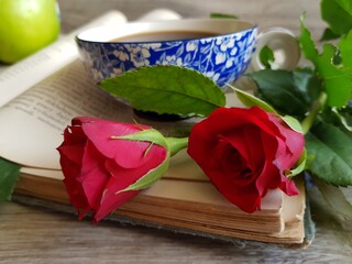 The cup of tea on the old book with red roses.