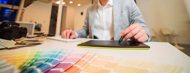 Photographer-designer works at a table, holds a stylus of a graphic tablet in the river