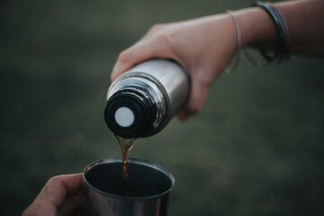 Drinking filter coffee in the park. Pouring coffee into the cup from the thermos with green background with no people. Coffee love concept. Camping concept.