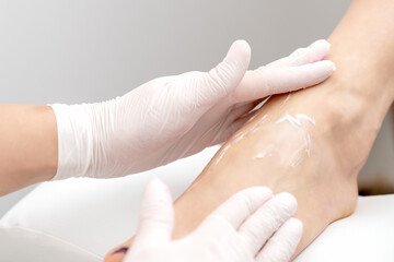 Human hands in protective gloves doing foot massage with moisturizing or peeling cream in eauty salon