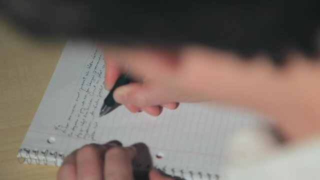 Person writing letter on ruled notebook paper in spiral binder with pen. Over the shoulder view of man writing letter with pen and paper. 