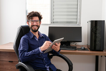 Hispanic man in his office using tablet looking at camera smiling. Home office concept.