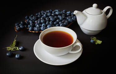 Still life, cup with tea, teapot, blueberry and dry leaves of mellisa on dark background