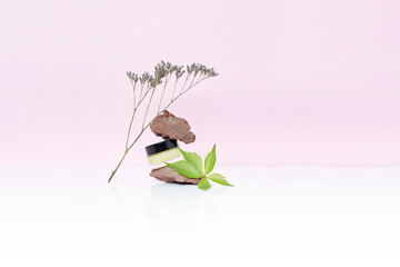 Obraz premium Cosmetic jar with yellow butter or cream with natural volcano stones and flower on white and pink background. High quality photo