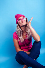Naklejka premium young pretty teenage modern hipster girl posing emotional happy on blue background, wearing pink hat and glasses, lifestyle people concept
