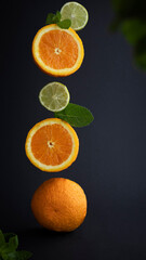 Flying halves of oranges and limes with mint on a dark background, copy space