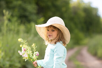 childd girl with field flowers in a straw hat in the field