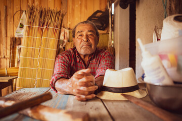 Old artisan in a local community of Garopaba, Brazil. Craftsman resting at his wooden workshop. Elder wearing red plaid shirt