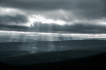 Fototapeta na wymiar Landscape from a mountain viewpoint into the winter mountain nature with dramatic contast light and winter scenery. Strong light rays in the clouds. Harz Mountains, Harz National Park in Germany.
