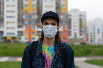 Handsome young man in regular disposable surgical, medical mask on the street in the city....