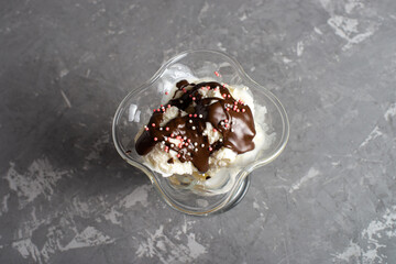 White balls of vanilla ice cream with chocolate topping and in sprinkles a dessert glass. Decorated ice cream on a table made of dark, rough concrete. Copyspace flatlay.