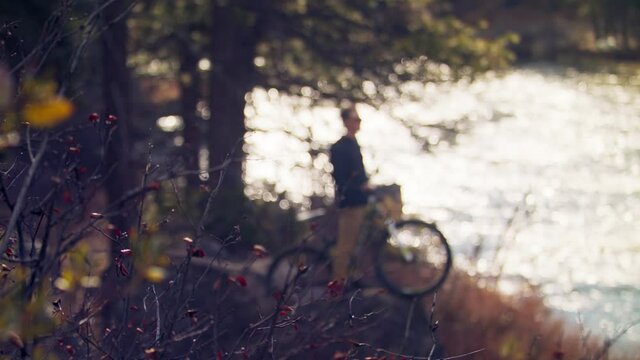 Teenager with mountain bike admiring view of flowing river in daylight