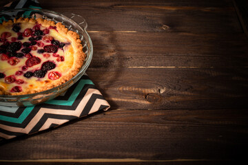 Baked round homemade cheesecake with berries is on a striped napkin. Pie on an old dark wood table. Flatley with copyspace.