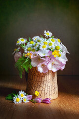 Still life with small wildflowers in a ray of light. Bouquet of wildflowers in a clay vase.