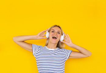 Beautiful girl DJ listening music in white headphones on a yellow background and having fun. Touch her headphones, smiling with wide opened mouth