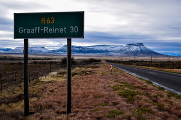 Road sign on an open road with snowy mountains in the background.