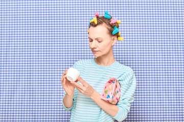 Girl with colorful hair curlers on head is holding jar of face cream