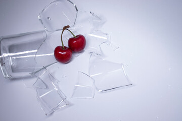 pieces of broken glass are scattered on a gray-white background with a cherry on it. High quality...