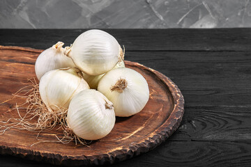 white onions on a wooden board on black background