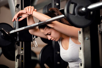 Very beautiful teenage girl resting and getting motivated between sets of barbell squats in gym....