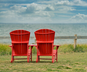 Two red Adirondack chairs overlooking the ocean in PEI National Park, Prince Edward Island.
